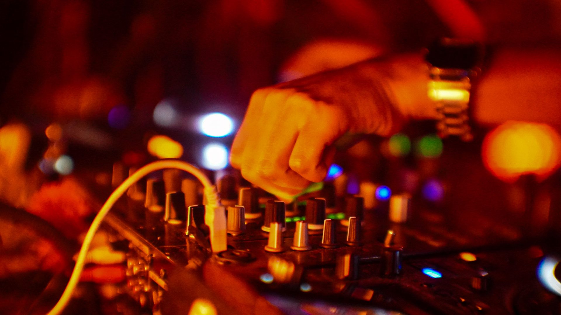 Close-up of a DJ's hand working the mixer decks under club lights