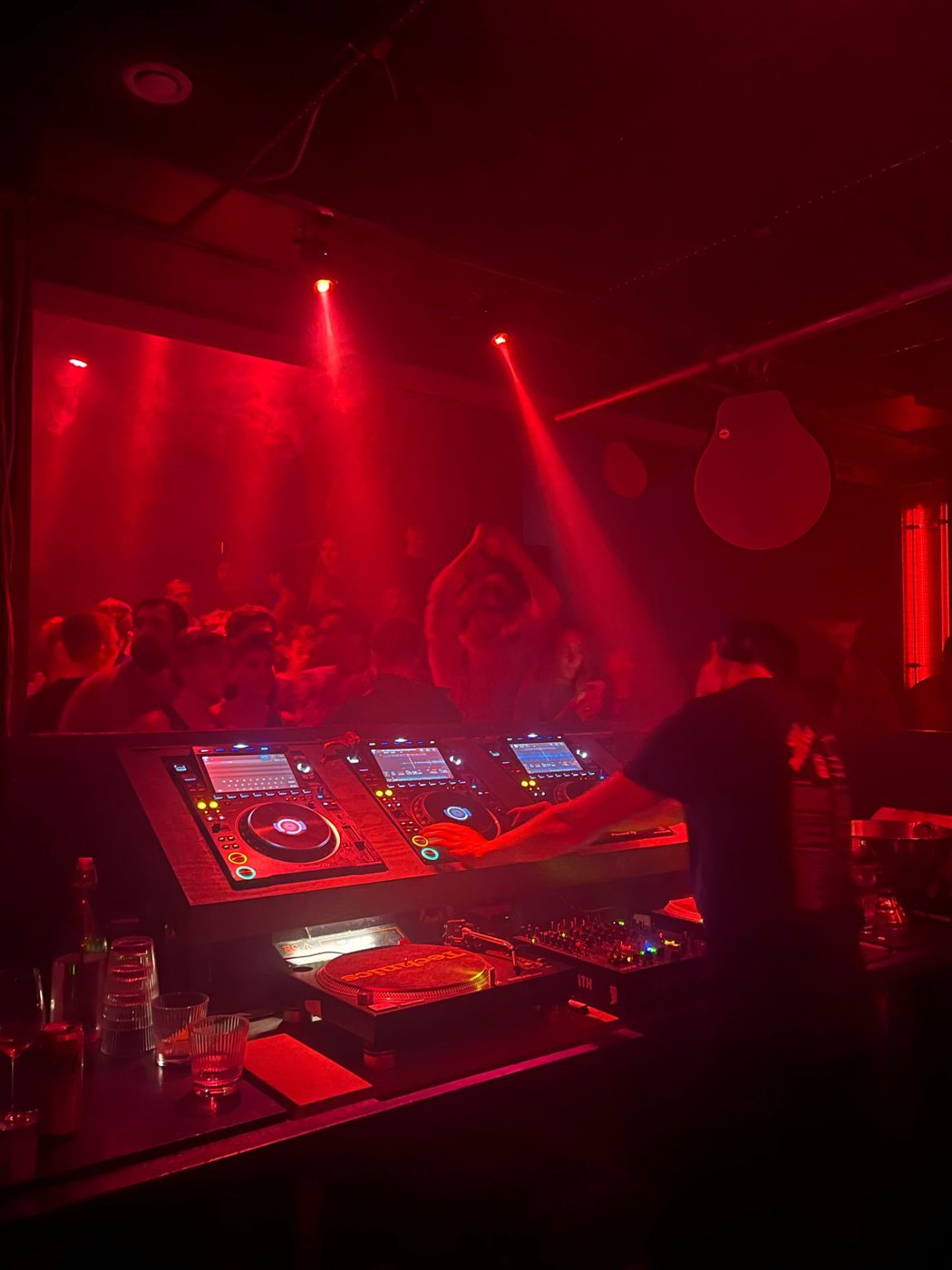 DJ behind the decks in a red-lit nightclub with a dancing crowd